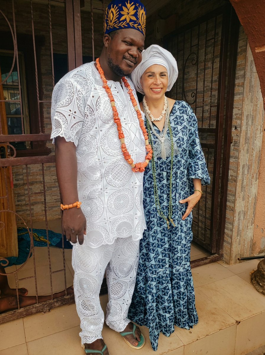 Babalawo Akin Alapo in white lace agbada and coral beads beside a visiting devotee